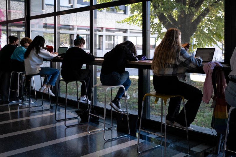 Auf dem Bild sind Schülerinnen zu sehen, die vor einer Glasfront an ihrem Laptop arbeiten und nach draußen schauen.