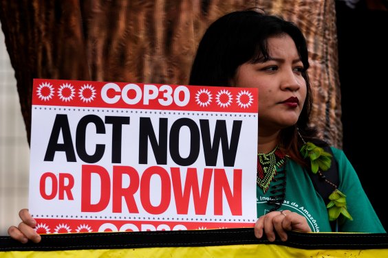 Eine indigene Frau protestiert für mehr Klimaschutz bei COP30 Eine indigene Frau hält ein Plakat hoch mit der Aufschrift COP30: Act Now or Drown.